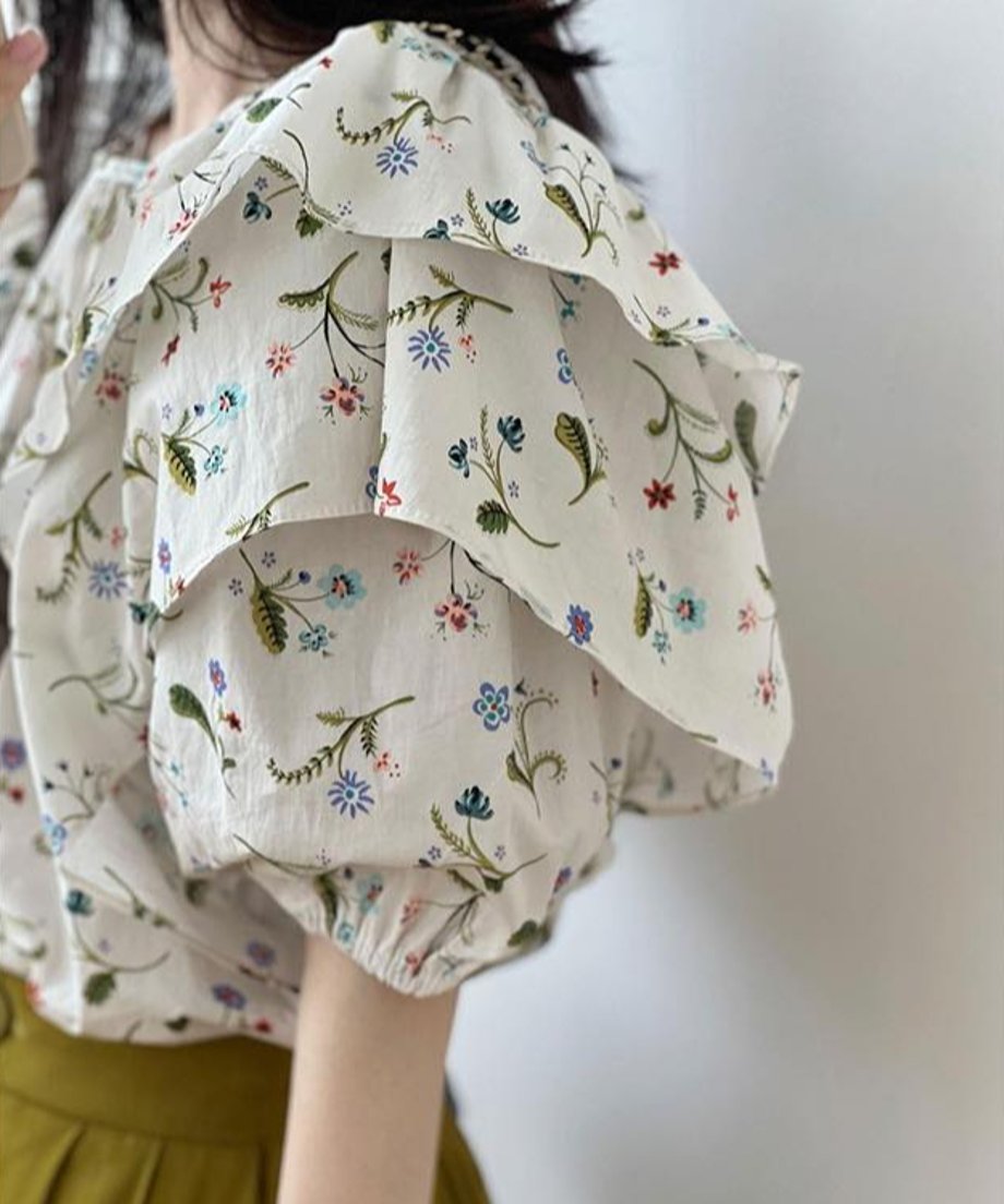 花柄がプリントされたラッフル袖ブラウスを着た女性のバストアップ。カーキ色のワイドパンツを着用。