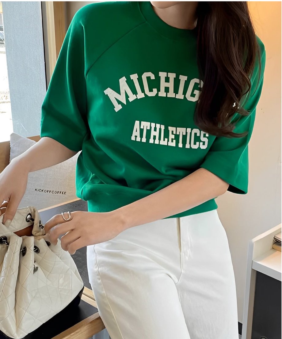 グリーンのロゴTシャツを着た女性、白いパンツとのコーディネート。