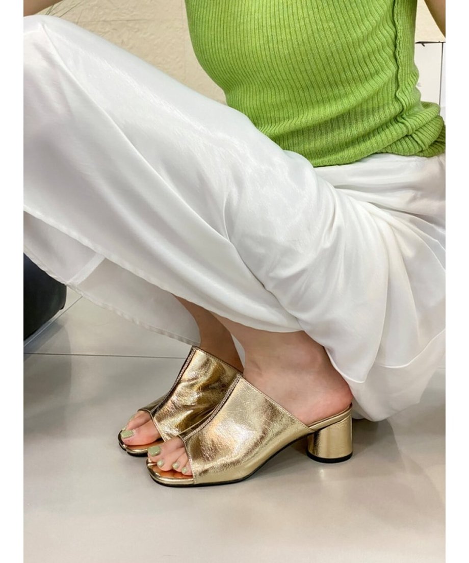 ゴールドのミュールを着用したしゃがんでいる女性の足元のアップ。