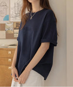 ネイビーのロゴTシャツを着た女性が、室内でリラックスした様子。白いスカートとコーディネート。