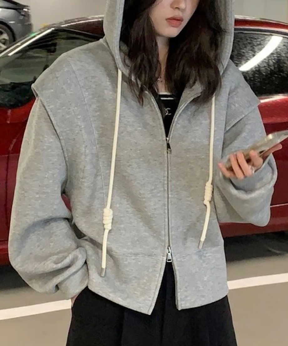 グレーのダブルジップデザインフーディを着用し、スマートフォンを持つ女性。正面から見た、肩の落ち感とフードのボリュームがわかるカット。