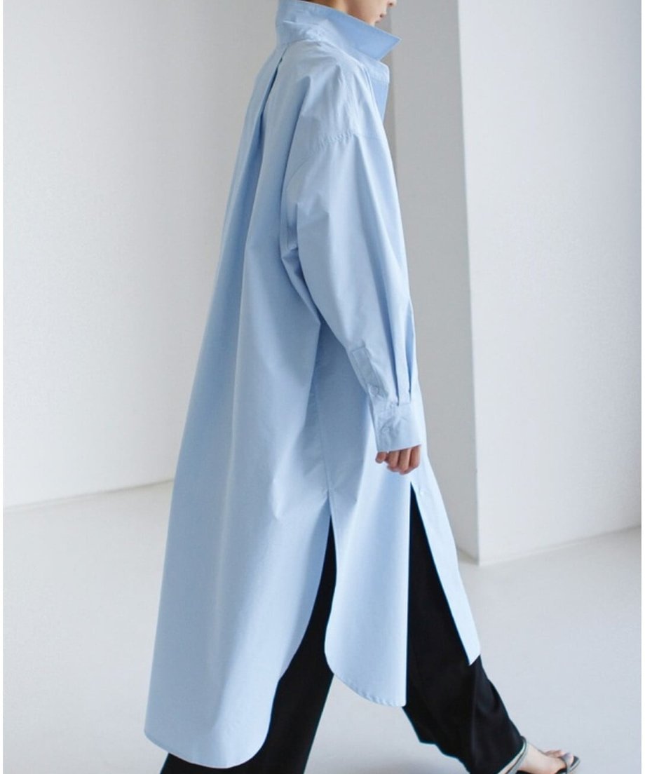 ブルーのアシンメトリー丈ロングシャツを着用した横姿。袖のボリュームとスリットのバランスが美しい。