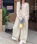 屋外で立ちポーズをとる女性。ベージュのバギーワイドオーバーオールに、長袖Tシャツをインナーにし、黄色のミニバッグとスマートフォンを持っている。髪の毛は三つ編みにリボンを付けている。