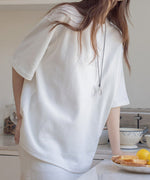 オフホワイトのTシャツを着た女性がキッチンで立っている様子。