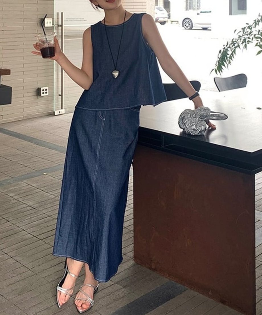 テラス席でシルバーのバッグを持ち、デニムのスリーブレスセットアップを綺麗に着こなして立つ女性の全身像。