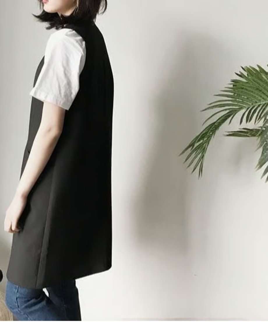 女性が白いTシャツとデニムに黒のロングベストを着用している、側面からのアップ。