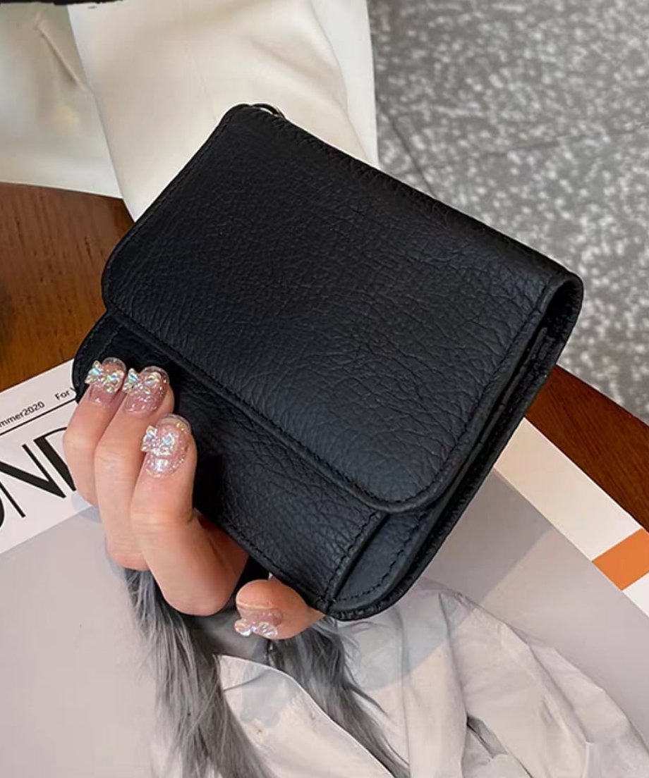 黒色のシボ感がある三つ折りミニウォレットを持つ女性の手元
