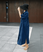 ブルーのリネンドレスワンピースを着用した女性が黒のハットを合わせて歩いている様子