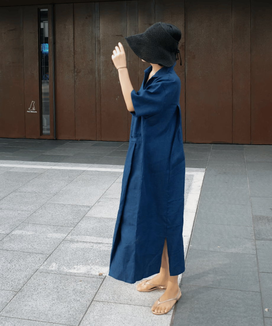 ブルーのリネンドレスワンピースを着用した女性が黒のハットを合わせて歩いている様子