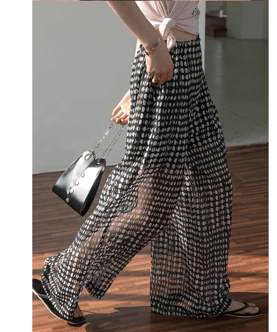 ハイウエストのドット柄ワイドパンツを着用し、黒のハンドバッグを持って歩く女性の足元。動きに合わせて揺れる生地の質感を強調。