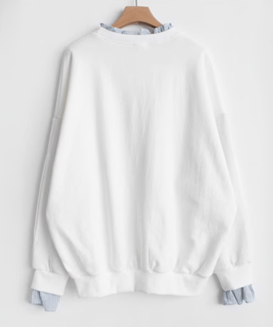 ホワイトのレイヤードスウェットをハンガーにかけた背後の商品画像。ゆったりとした背中と裾のリブ、ストライプの袖口フリルが見える。