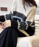 アイル柄ニットを着用し、白いソファに座った女性のクローズアップショット。袖口のアイボリーと黒の配色が強調されています。