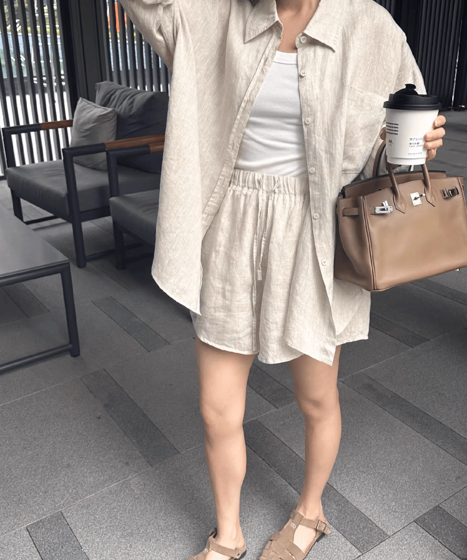 リネンのセットアップを着た女性がバッグとコーヒーカップを持っている。