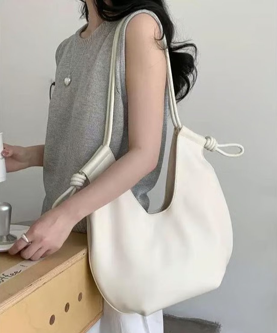 白いトップスとシルバーのネックレスを着用した女性が、ホワイトのノットデザインショルダーバッグを肩にかけている様子。