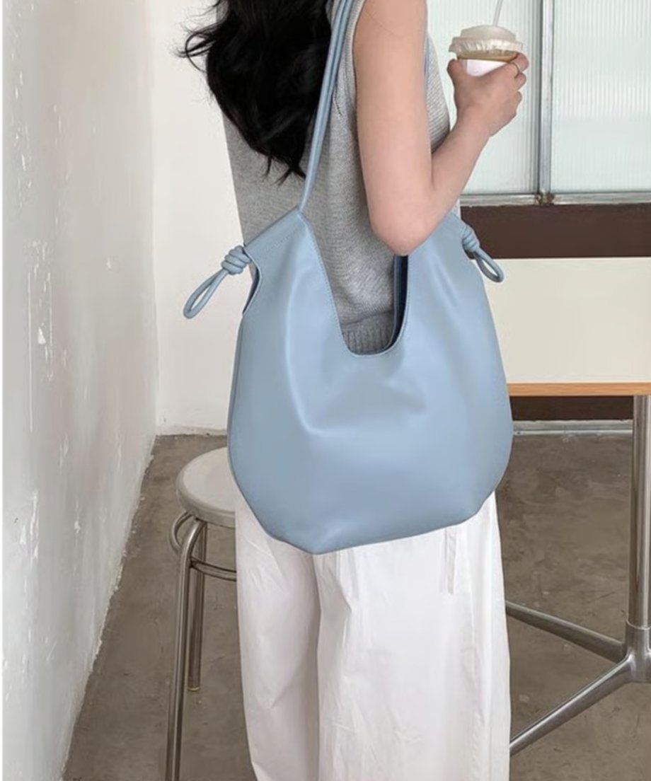 色のノースリーブと白いワイドパンツを着用した女性が、ライトブルーのノットデザインショルダーバッグを肩にかけている様子。