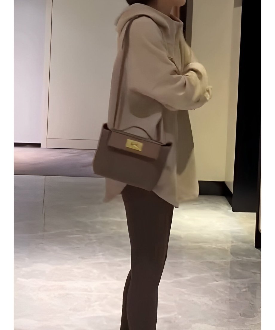 オフホワイトのオーバーサイズフーディーを着用し、茶色のレギンスを合わせた女性が、斜めがけのミニバッグを持って立っている。