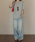 グレーのロゴTシャツとライトブルーのワイドデニムを着用した女性のコーディネート。