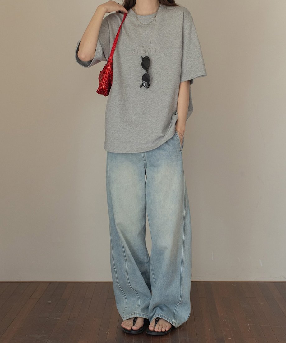 グレーのロゴTシャツとライトブルーのワイドデニムを着用した女性のコーディネート。