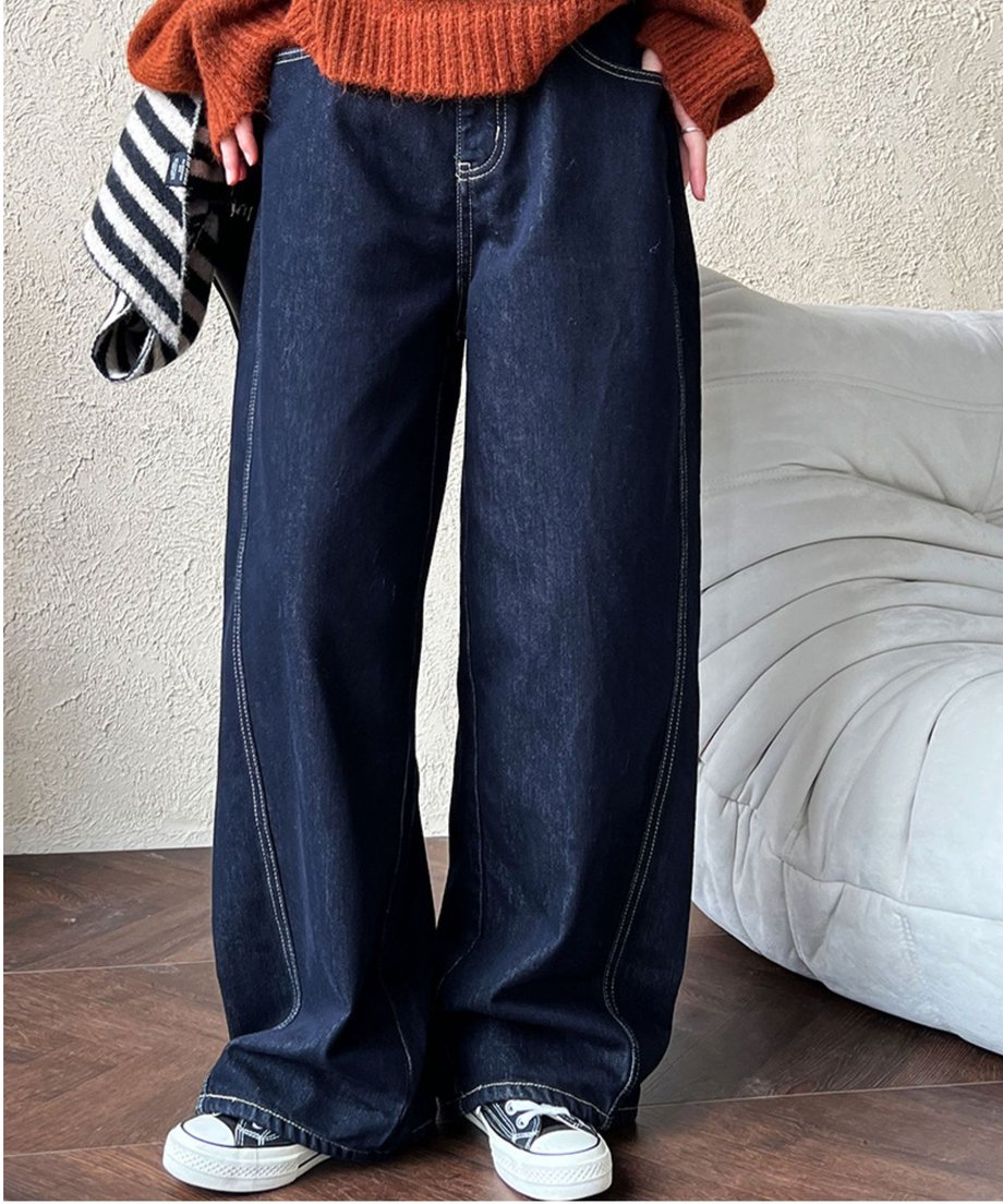 テラコッタ色のニットとダークブルーのワイドデニムパンツを着用し、両手をポケットに入れている女性。足元は白のハイカットスニーカー。