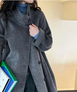 ダークグレーのスタンドカラーコートを着用した女性の上半身アップ。スタンドカラーのボタンディテールと水色のタートルネックインナーが見える。