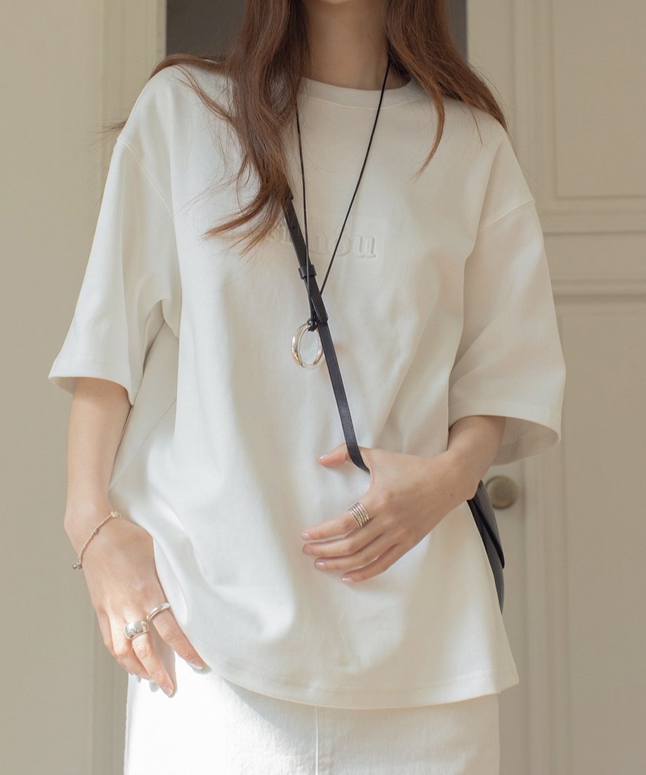 オフホワイトのTシャツを着た女性が黒いショルダーバッグを着用している様子。