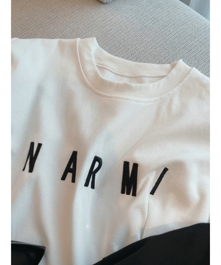 ホワイトのTシャツ生地に施された、光沢のある黒い立体刺繍ロゴ「NARMI」のクローズアップ。
