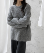 グレー色のふわふわしたクルーネックニットを着用し、腕を組んでいる女性のバストアップ。黒いパンツを着用。