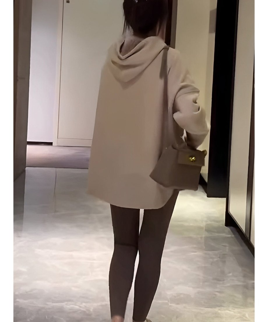 オフホワイトのフーディーを着た女性の後ろ姿。ゆったりとした身幅と、ヒップを覆うの長めのラウンドカットされた裾が確認できる。