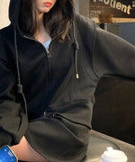 ブラックのダブルジップデザインフーディを着用し、椅子に座った女性のショット。裾のラインがカーブを描いているのが特徴。