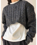 グレーのツイスト編みクロップドニットを着用した女性。インナーの白Tシャツとのコントラストが特徴的。