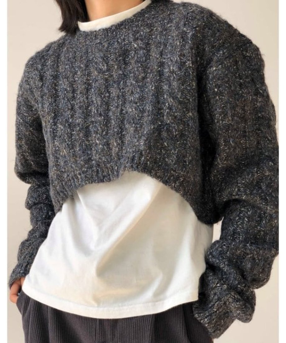 グレーのツイスト編みクロップドニットを着用した女性。インナーの白Tシャツとのコントラストが特徴的。
