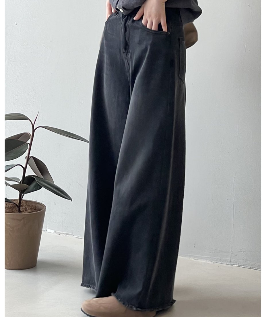 黒の超ワイドデニムパンツとグレーのトップスを着用し、手をポケットに入れた女性の全身。