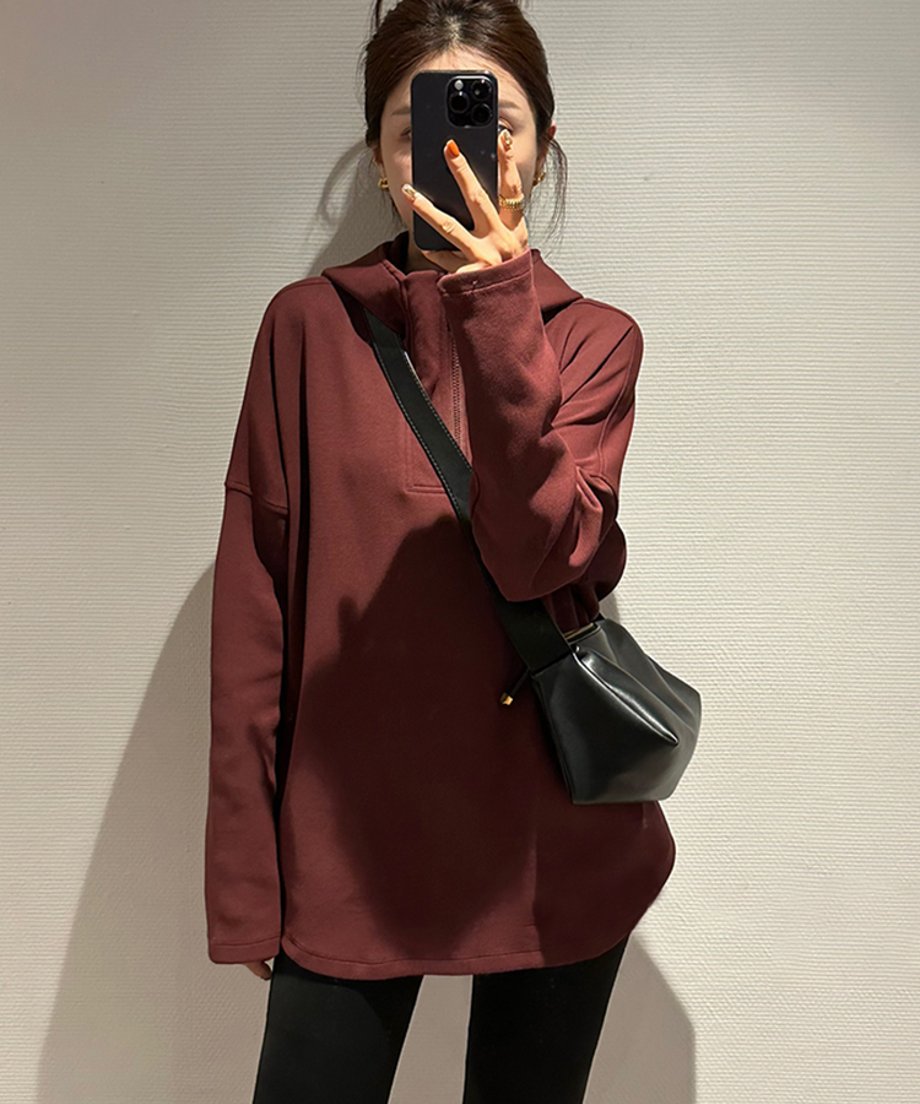 クラレットのハーフジップフーディーを着用し、携帯電話で自撮りしている女性。黒いレギンスと黒のミニショルダーバッグを合わせている。