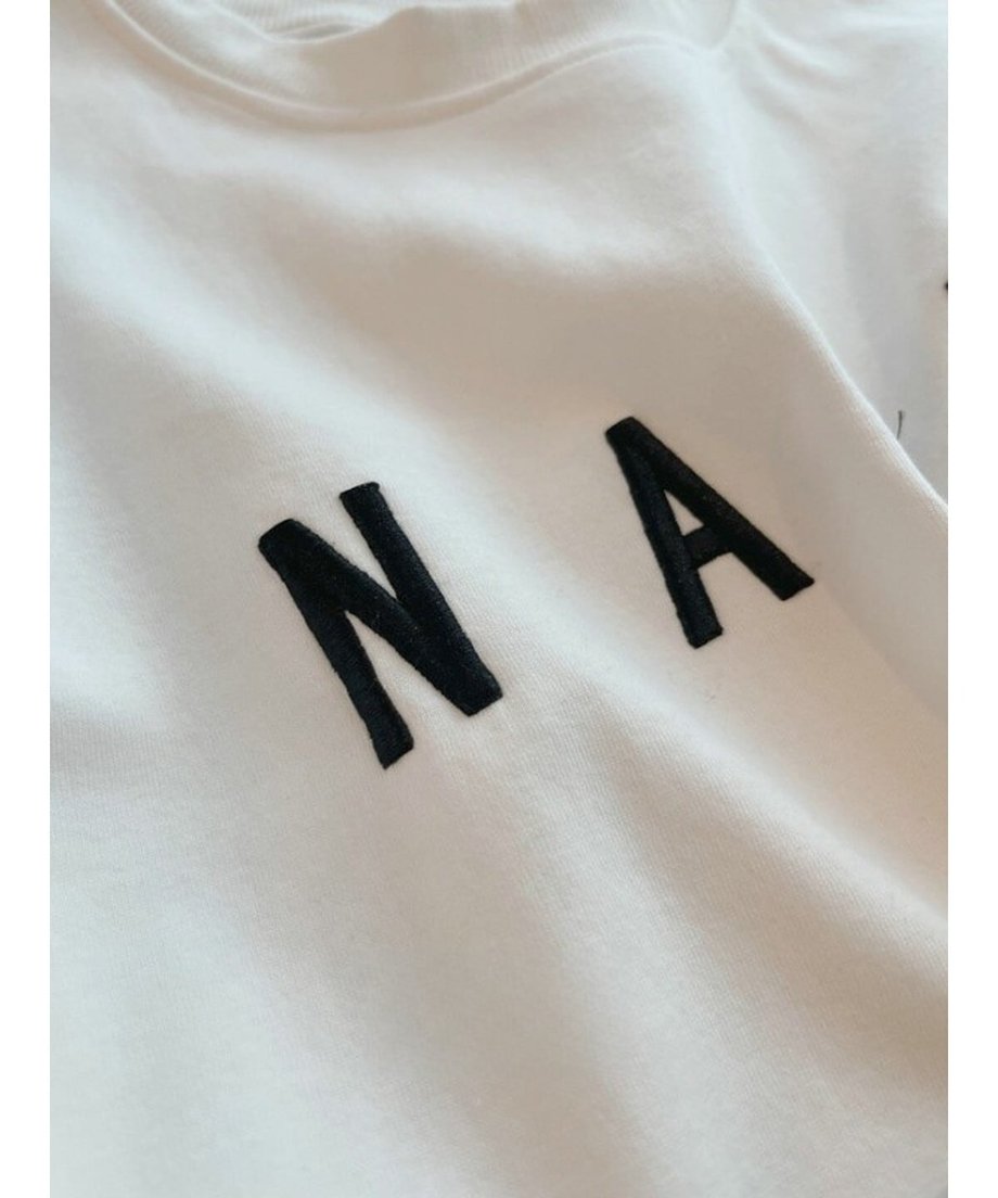 Tシャツの表面にある「N A」の文字の立体的な刺繍ディテールと質感。