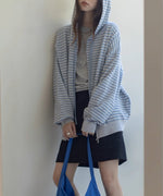 ライトブルーとグレーの細いボーダー柄のジップアップパーカーを着用した女性の半身。黒いミニスカートを合わせている。