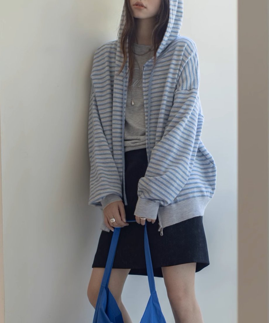 ライトブルーとグレーの細いボーダー柄のジップアップパーカーを着用した女性の半身。黒いミニスカートを合わせている。