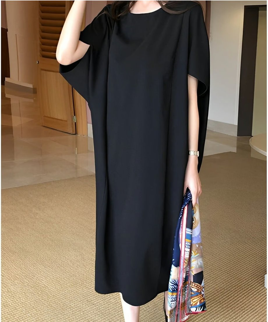 ワイドな袖のデザインが特徴的な、ブラックのルーズシルエットワンピースを着用した女性の立ち姿。
