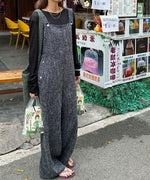 ブラックのワイドレッグオーバーオールを着用し、街角の売店前に立つ女性の全身カット。