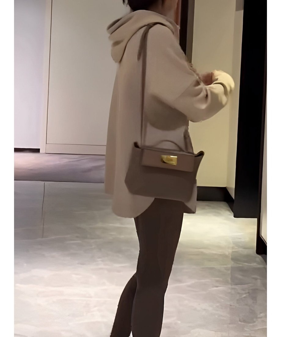 オフホワイトのオーバーサイズフーディーを着用し、茶色のレギンスを合わせた女性が、斜めがけのミニバッグを持って立っている。