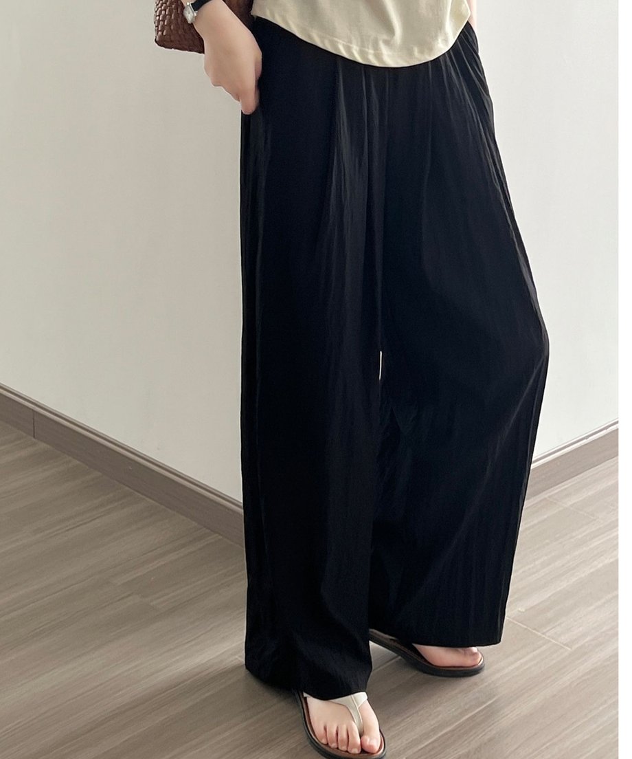 ブラックのプリーツワイドパンツを着用した女性の、腰から足元まで。アイボリーのトップスとサンダルを合わせている。