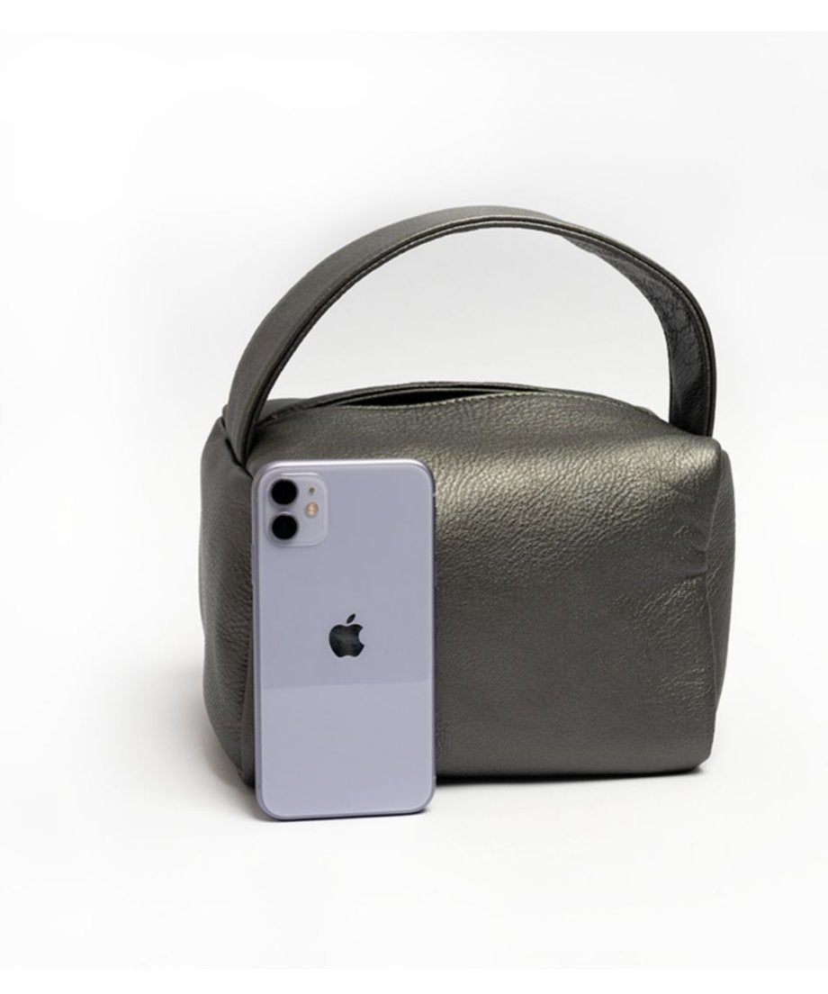 白い背景に、パールグレーのレザーハンドバッグの横に、サイズ比較としてiPhoneが置かれている画像。