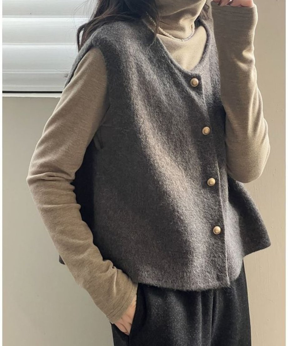 グレーのニットベストを、ベージュのタートルネックトップスに重ね着した女性の上半身のショット。