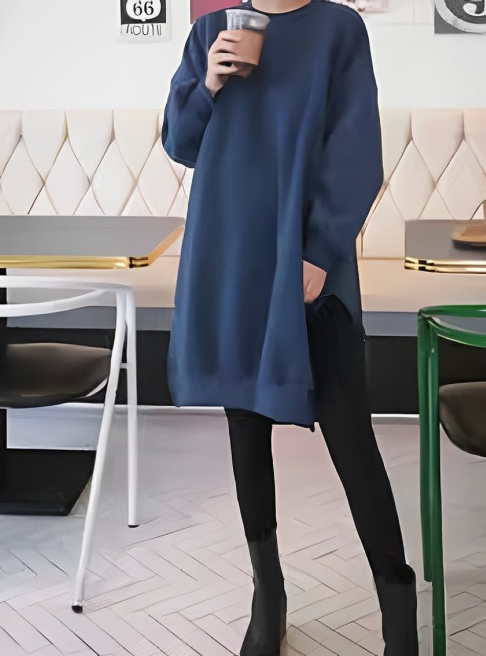 ブルーのオーバーサイズスウェットシャツを着た人物がカフェで飲み物を持っている。