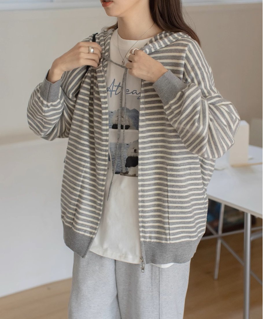 グレーと白の細いボーダー柄のジップアップパーカーを着用した女性の半身。インナーには白い柄のTシャツ、ボトムスにはライトグレーのスウェットパンツを合わせたカジュアルな着こなし。