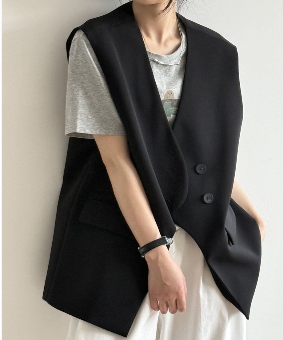 黒のテーラードジレに、グレーのプリントTシャツ、白のボトムスを合わせた女性の正面。