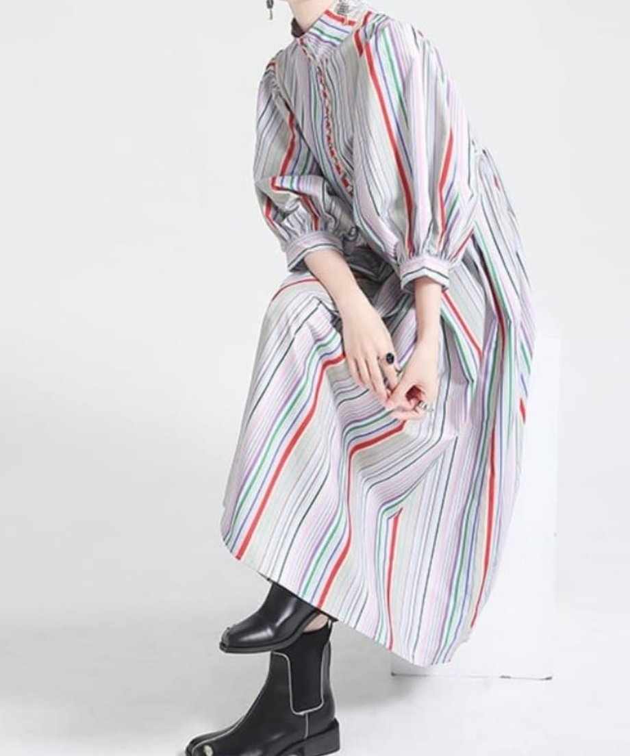椅子に座った状態の着用画像。裾の広がりと、流れるようなストライプ柄ワンピースのシルエット。