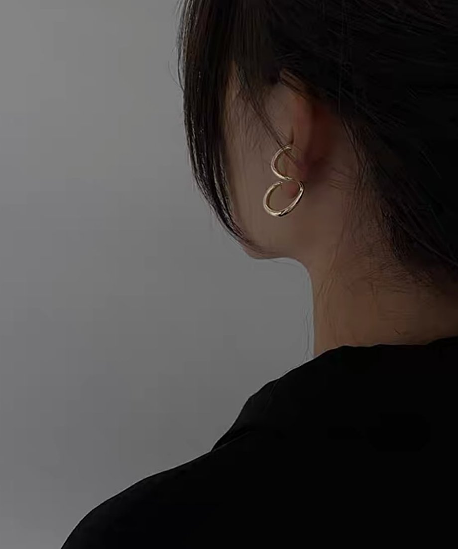 黒いトップスに合わせた、モードな雰囲気のゴールド変形ピアスをつけた女性。