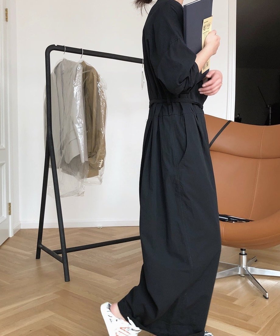 黒のラップオールインワンを着用した女性の横向き全身ショット。手でノートまたは本を抱えている。