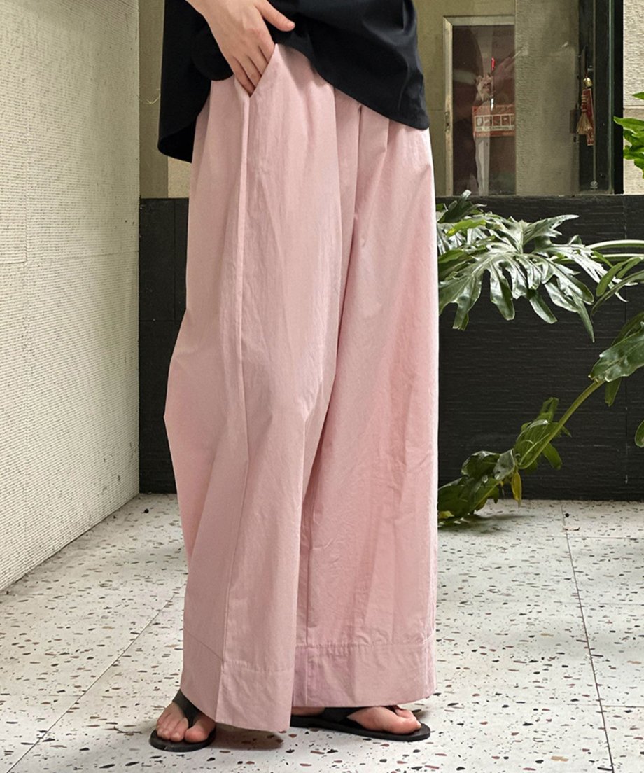 ピンクのワイドレッグパンツを着用し、黒のトップスを合わせた女性の、屋内のテラスでの下半身全身