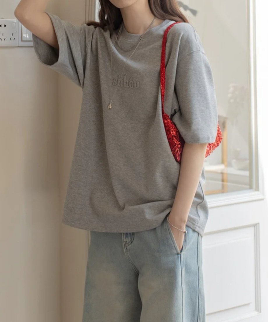 グレーのTシャツを着た女性が赤いバッグを持っている様子。